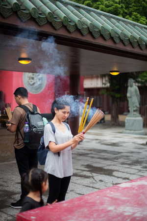 Asian girl praying outdoor at a temple, offering incense sticksのeditorial素材