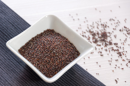Black mustard seeds in a white bowl and light backgroundの写真素材