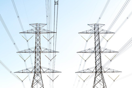 a highvoltage electricity pylons against blue sky and sun raysの写真素材