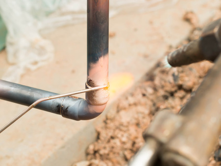 Plumbing contractor works sweating the joints on the copper pipe domestic water system on a luxury...