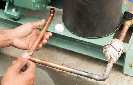 Plumbing contractor works sweating the joints on the copper pipe domestic water system on a luxury...