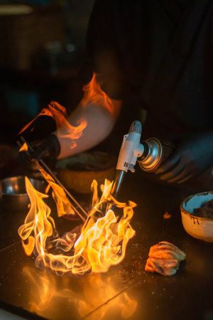 Close-up of the hands of a caucasian man in a black T-shirt and black jeans working with a torch in a kitchenの写真素材