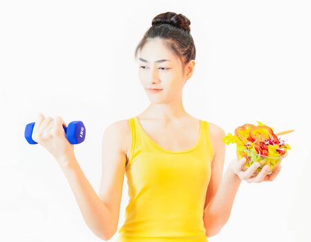 A young, beautiful asian woman, smiling, cheerful, carrying a small red tomato. And a salad cup placed on the front table take care of your health Eating a homeopathic dietの写真素材