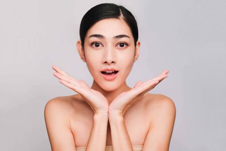 young beautiful asian woman with clean and bright skin, Cosmetic Beauty Concept,hands touch on the cheek, smiling and friendly face isolated on grey backgroundの写真素材