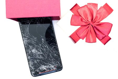 The mobile phone on the screen is broken, the device is off, cannot be opened isolated on white background with Gift box and red ribbon Selective focusの写真素材