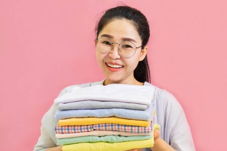 Modern Electric iron and stack of clothes on ironing board on pink background in laundry room....