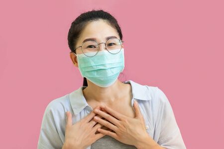 Young asian woman wore a gray undershirt, Blue shirt and protective masks against virus and air pollution,make gesture handful clasped and raised, isolated on pink background,health care conceptの写真素材