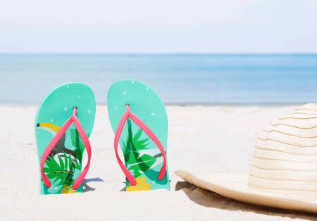 Green flip-flops embroidered on the sand and the hat at the sea with space of blue sky summer...