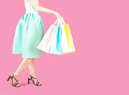 The back of woman low body part wore blue skirt and black high heels. Carrying a shopping bag in many pastel colors on pink background selective focusの写真素材