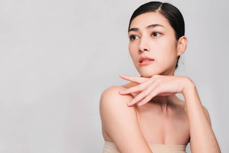 young beautiful asian woman with clean fresh skin, hands touch on the cheek, smiling and friendly,face care, facial treatment, Cosmetology, beauty and spa,isolated on grey backgroundの写真素材