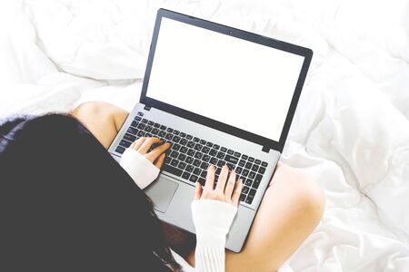 Selective focus a body part of young asian woman wear white knitwear dress and socks on bed,work online lifestyle with blank screen laptop relax at home ,white blanket copy spaceの写真素材