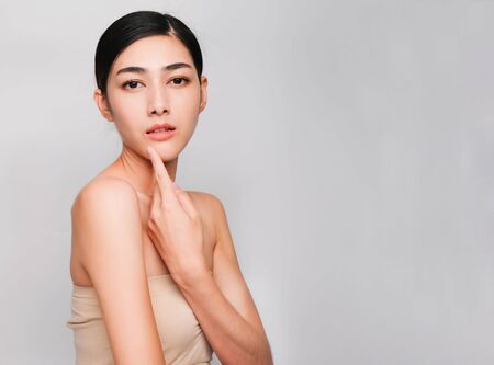 Beautiful asian woman ,young asian girl with clean and bright skin, Cosmetic Beauty Concept,hands touch on the cheek,smily and friendly face isolated on grey backgroundの写真素材