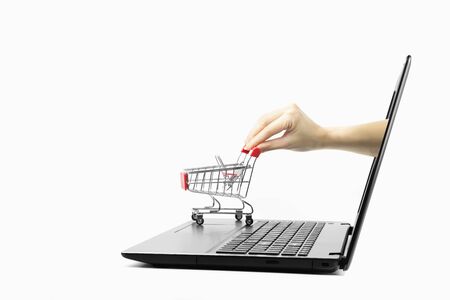 The hand extends from the laptop screen to the red shopping cart isolated on white background with copy spaceの写真素材
