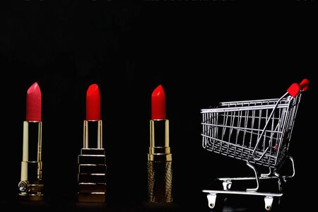 Red lipstick, gold bars and shopping cart isolated on black background with copy spaceの写真素材
