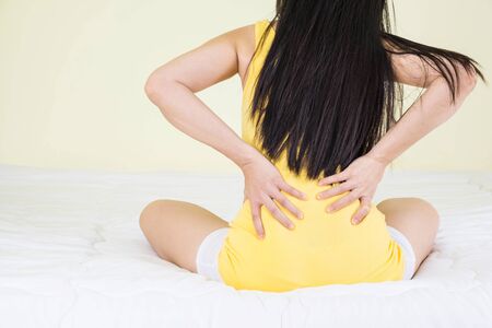 Back view of young woman suffering from Backache or Sore waist after her wake up in the bedroom....