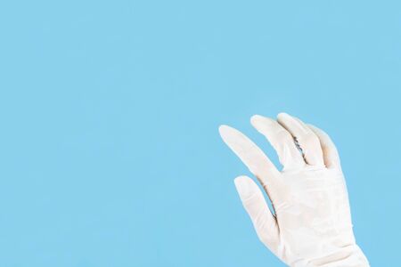 White latex medical gloves on a woman's hand outstretched isolated on blue backgroundの写真素材