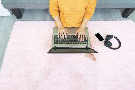Selective focus young woman sitting in living room on pink carpet typing on keyboard,work online...