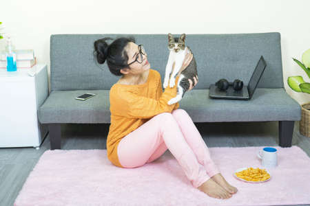 selective focus young beautiful asian woman wore orange knitwear,sitting in living room,playing with a cat,relax at home under quarantineの写真素材