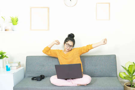 people and leisure concept -young beautiful asian woman wore glasses, sitting on gray sofa in living...