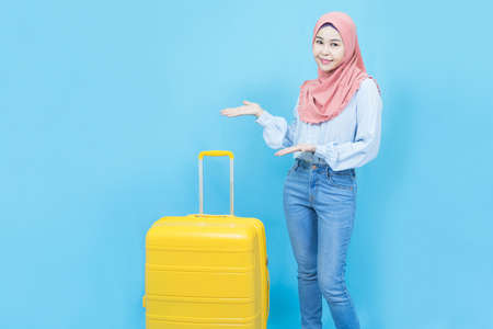 Portrait of young beautiful asian business muslim woman in traditional dress wearing medical face mask and black suit holding document isolated on blue backgroundの写真素材