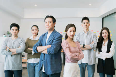 Group Portrait of young asian businesspeople standing indoors in office, looking at camera.Successful and confident business team with crossed armsの写真素材