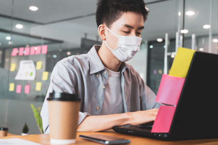 Young businessman working in office wearing protective mask for covid19 protection corona flu...