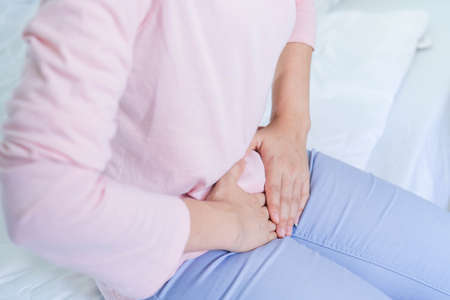 Gynecology concept. Hands of young woman on stomach as suffer from menstruation cramp, indigestion,...