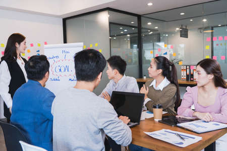 Young smart asian business female leader in a casual meeting with her teamwork colleagues at the modern design office presenting sales strategy plan and data or forecast for a project goal scheduleの写真素材