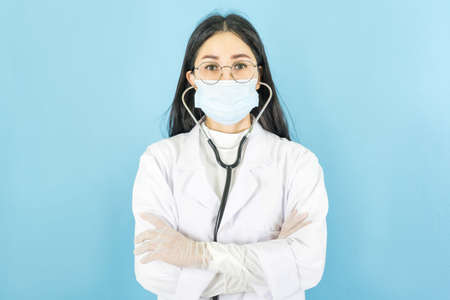 Confident woman doctor wearing medical mask standing with crossed arms. isolated female portrait on blue backgroundの写真素材
