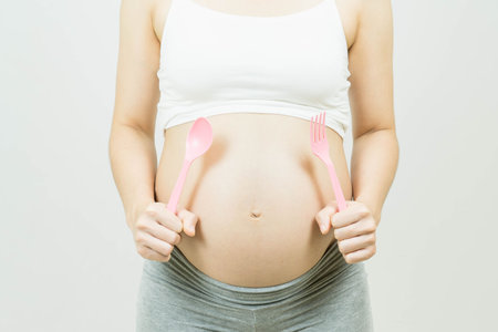 Pregnancy Cravings - A pregnant woman holding a spoon and forkの写真素材