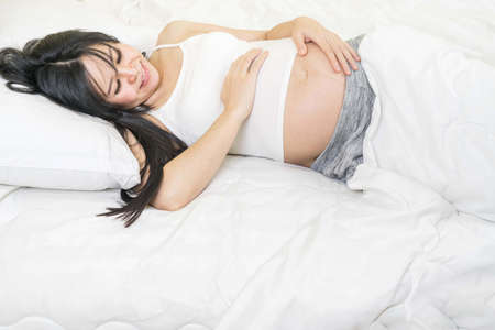 Happy smiling pregnant woman lying on her bed in her bedroomの写真素材
