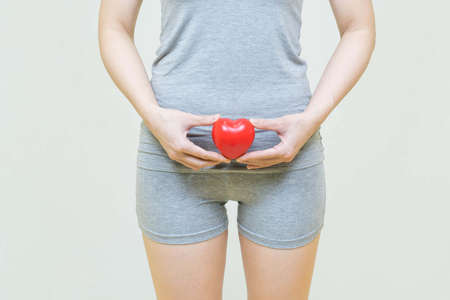 low body of woman standing over isolated gray background holding a red heart .health care concept.