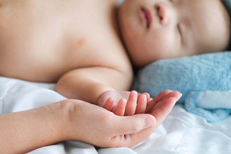 Selective focus hand of sleeping baby in the hand of mother close up on the bed, New family and baby protection from mom conceptの写真素材