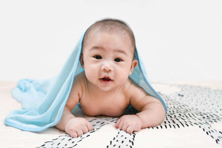 Asian baby under the towel after bathing at home lying on a bed under blue towel,Portrait of a crawling baby.の写真素材