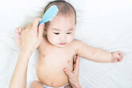 Mother's hand taking care of little boy. Mom giving baby a diaper change on bed.の写真素材