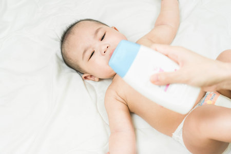 Mother's hand taking care of little boy. Mom giving baby a diaper change on bed.の写真素材