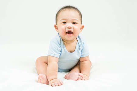 childhood and Childcare concept Portrait of cute little 5 months old  asian newborn baby boy wearing blue bodysuit sitting and smiling on white beedsheets.Selective focus.の写真素材
