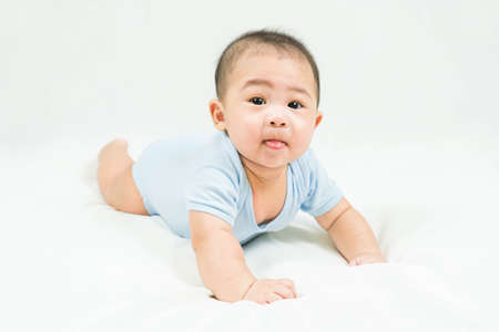 Childhood and Childcare concept Portrait of cute little 5 months old  asian newborn baby boy wearing blue bodysuit learn to crawl on white blanket at home.Smiling and looking camera.の写真素材