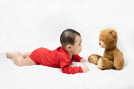 Little asian baby boy in red infant bodysuit and teddy bear on white background.Concept holiday Christmas, happy new year, infants, childhood.の写真素材