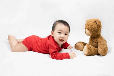 Little asian baby boy in red infant bodysuit and teddy bear on white background.Concept holiday Christmas, happy new year, infants, childhood.の写真素材