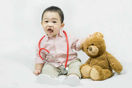 Adorable asian baby boy in pink shirt plays in doctor toy bear and red stethoscope.Health care and...