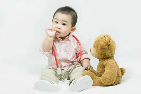 Adorable asian baby boy in pink shirt plays in doctor toy bear and red stethoscope.Health care and medical concept.の写真素材