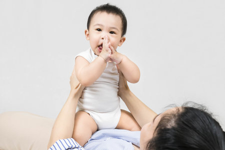 Motherhood Concept - Smiling young woman holding baby boy while lying on back, embracing Her Cute Infant Son, Loving Mom Enjoying Time With Her Baby.の写真素材