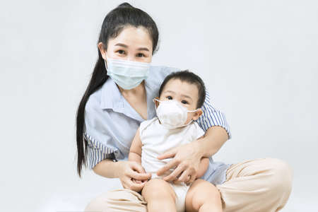 A mother in a protective mask with a baby is sitting at home in quarantine during the coronavirus and covid-19 pandemic.の写真素材