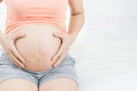 Young pregnant woman holds her hands on her swollen belly. hopeful and care baby in her body .Maternity prenatal care and woman pregnancy concept.の写真素材