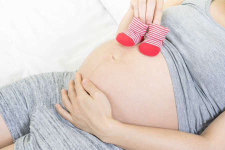 A tummy of a pregnant woman with red baby's bootees,Pregnancy health care preparing for baby...