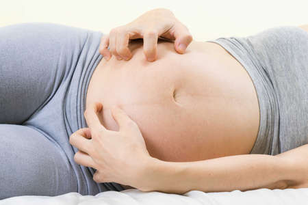 Pregnant woman scratching belly because itchy skin which causes striped- Pregnancy medicine concept.