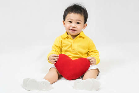 Asian cute baby boy about one year old in yellow shirt sitting and  smile with red heart shape...
