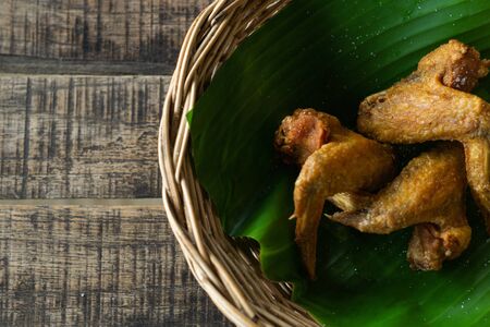Salt fried chicken on the banana leaf in a basket on wooden table top view. Favorite food from Thailandの写真素材