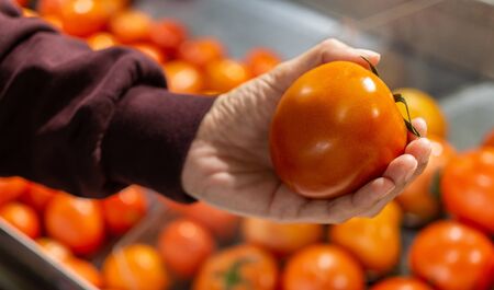 Women hand pick up tomato in supermarket.